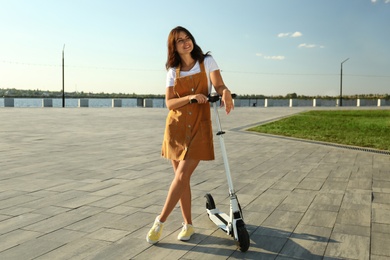 Young woman with modern kick scooter on waterfront