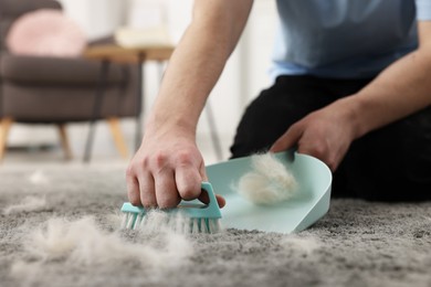 Photo of Man with brush and pan removing pet hair from carpet at home, closeup