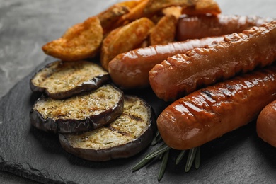 Photo of Delicious grilled sausages and vegetables on slate plate, closeup. Barbecue food