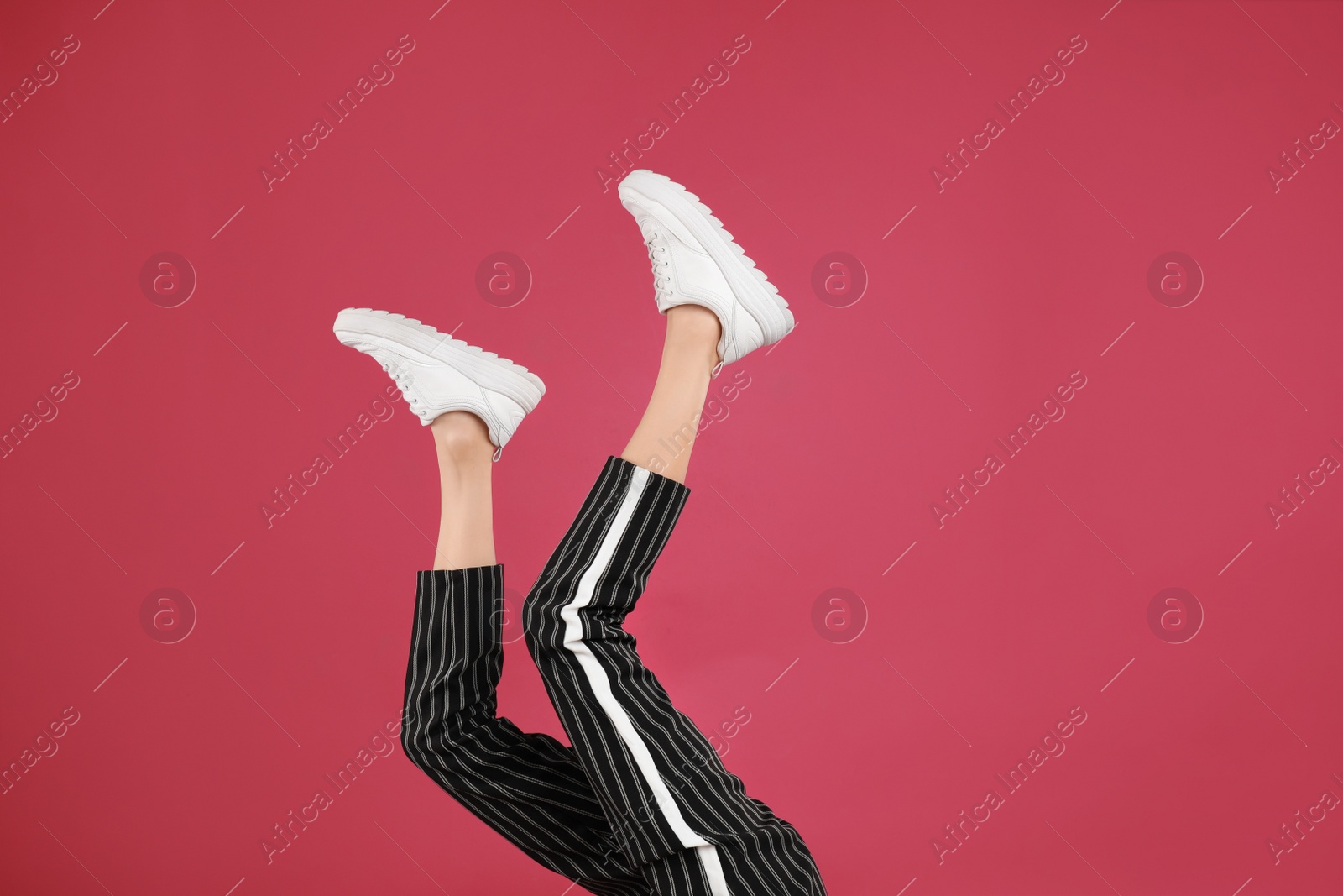 Photo of Woman in stylish sport shoes on crimson background