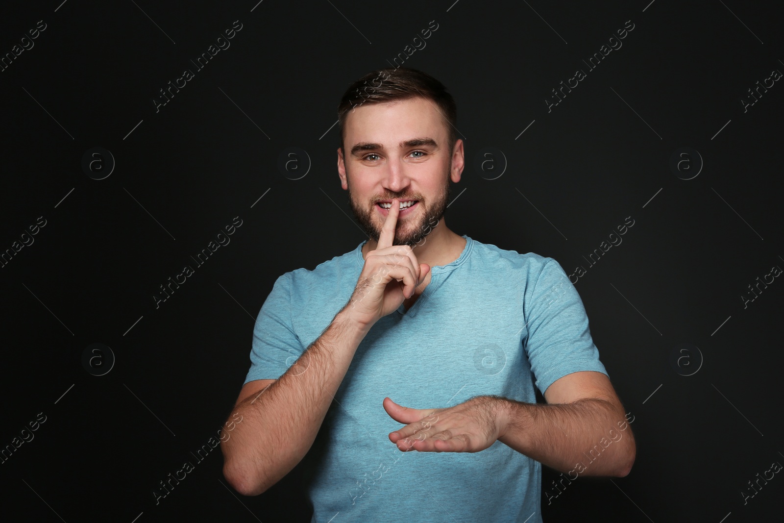 Photo of Man showing HUSH gesture in sign language on black background