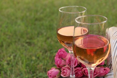 Photo of Picnic basket with glasses of delicious rose wine and flowers outdoors, closeup. Space for text