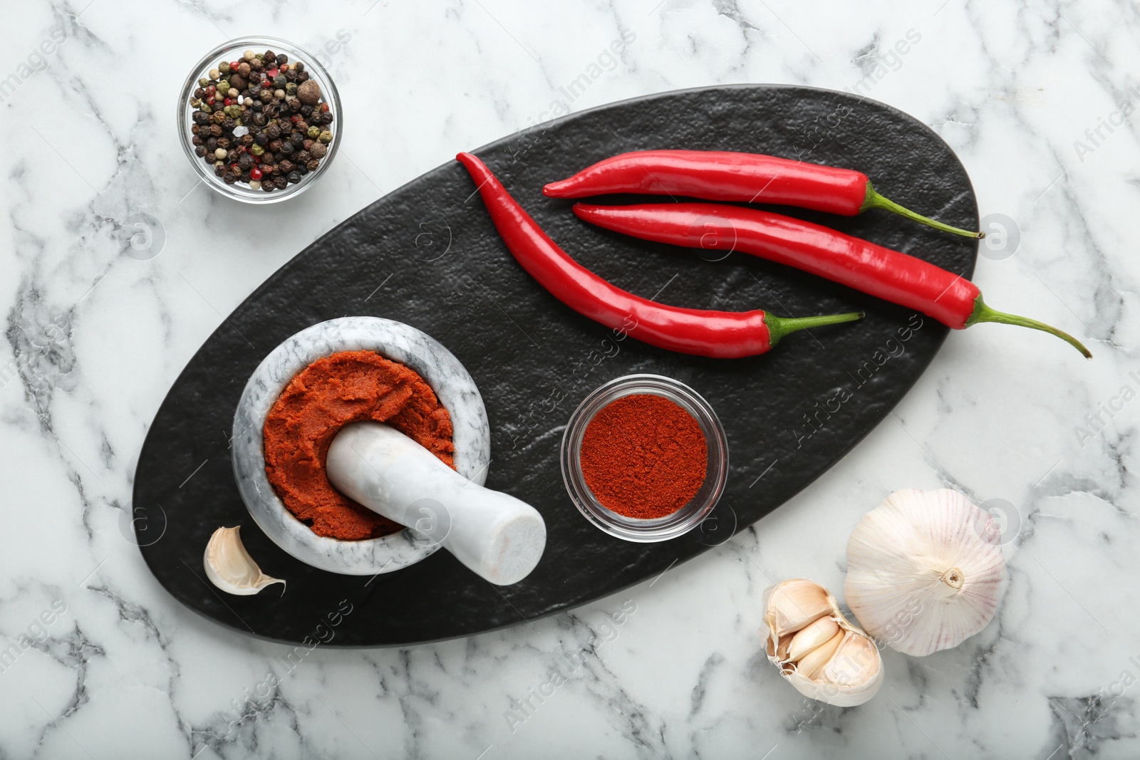 Photo of Red curry paste in mortar and ingredients on white marble table, flat lay