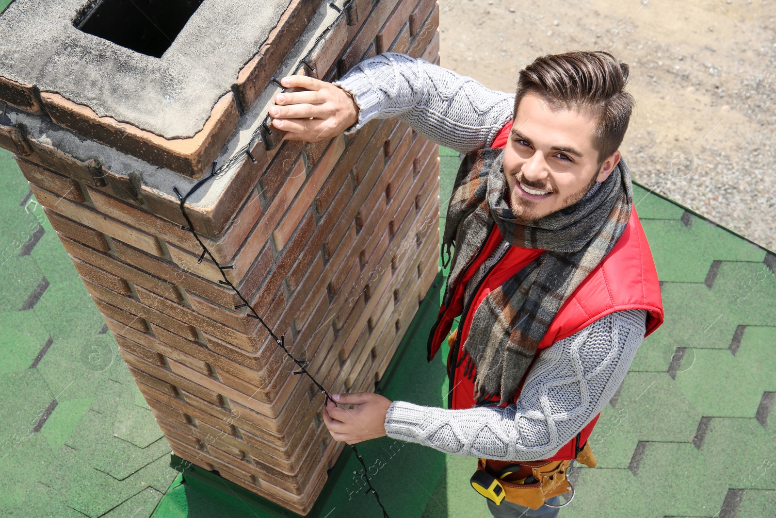 Photo of Young man decorating chimney with Christmas lights