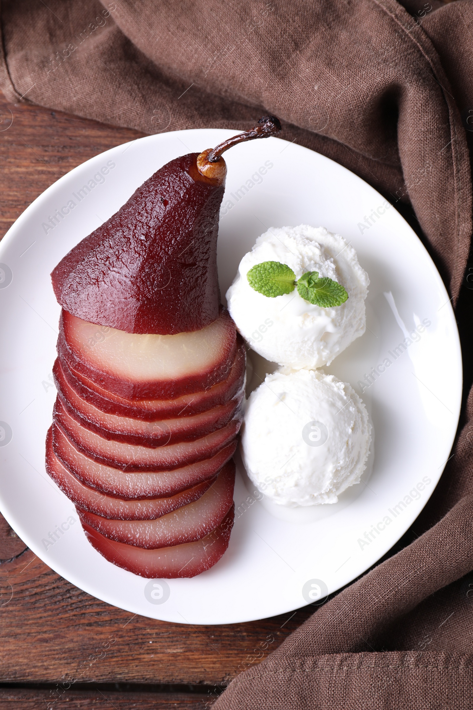 Photo of Tasty red wine poached pear and ice cream on wooden table, top view
