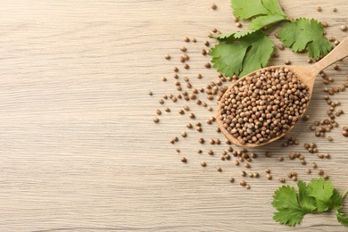 Spoon with dried coriander seeds and green leaves on wooden table, flat lay. Space for text