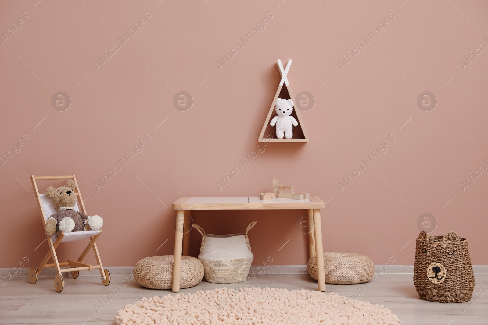 Photo of Cute child room interior with furniture, toys and wigwam shaped shelf on pink wall