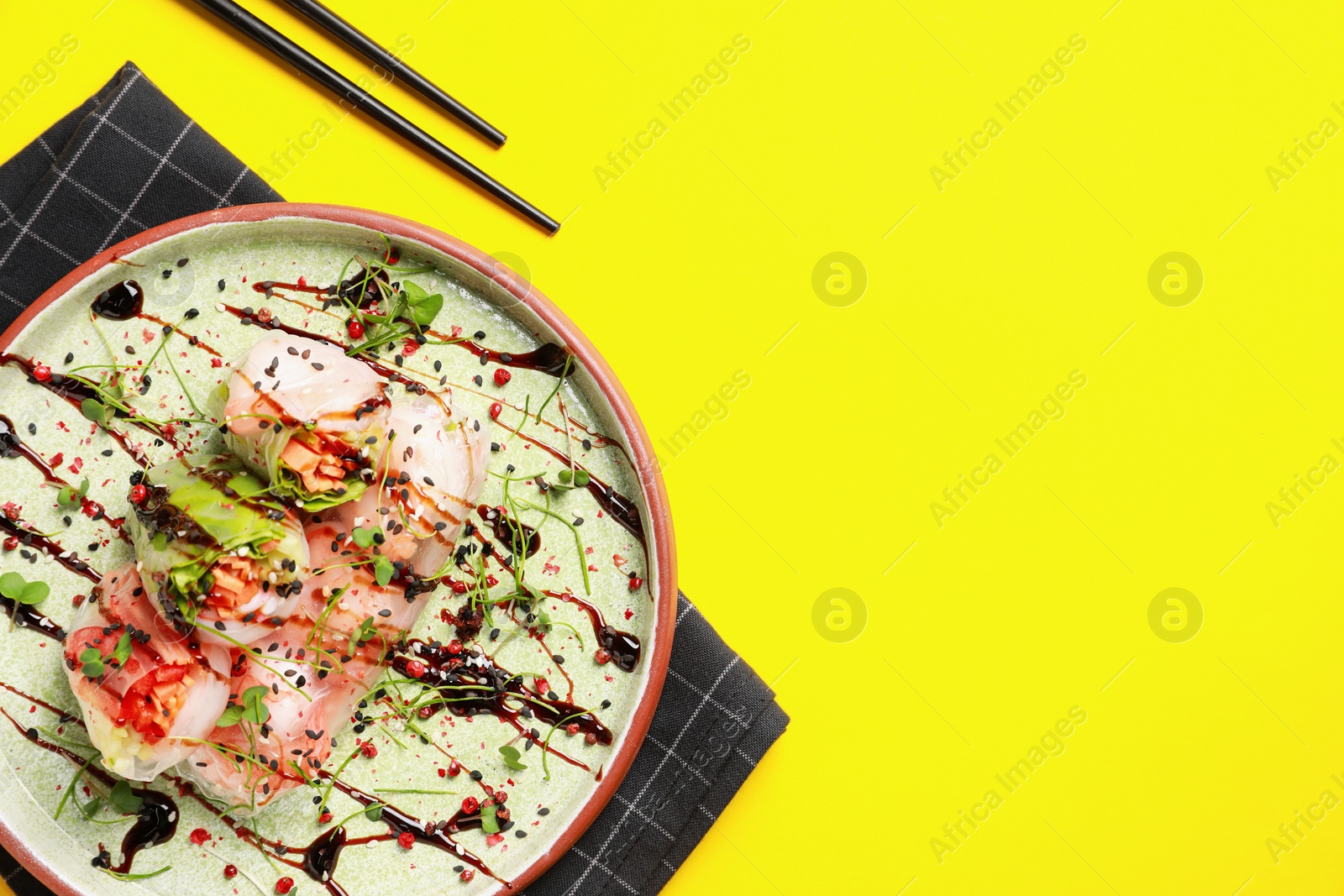 Photo of Delicious spring rolls with sauce, microgreens and chopsticks on yellow background, flat lay. Space for text
