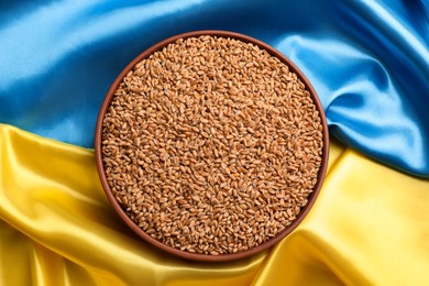 Bowl of wheat grains on Ukrainian flag, top view