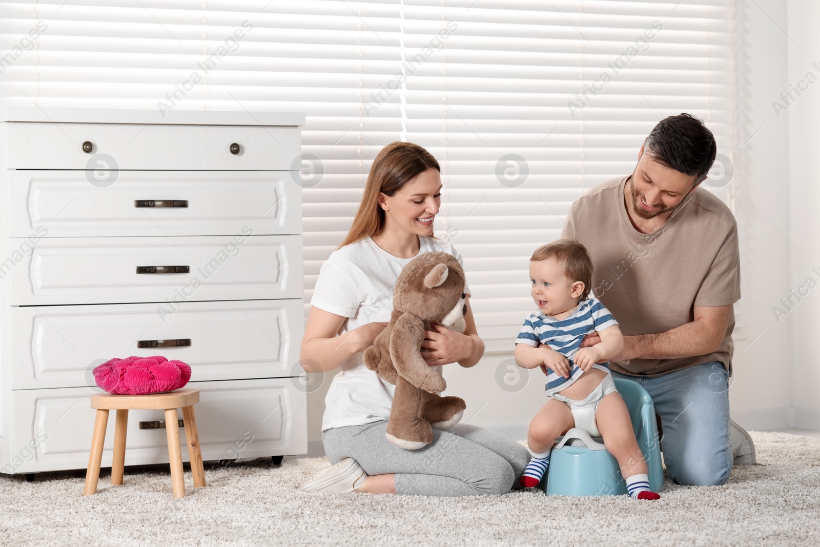 Photo of Parents training their child to sit on baby potty indoors. Space for text