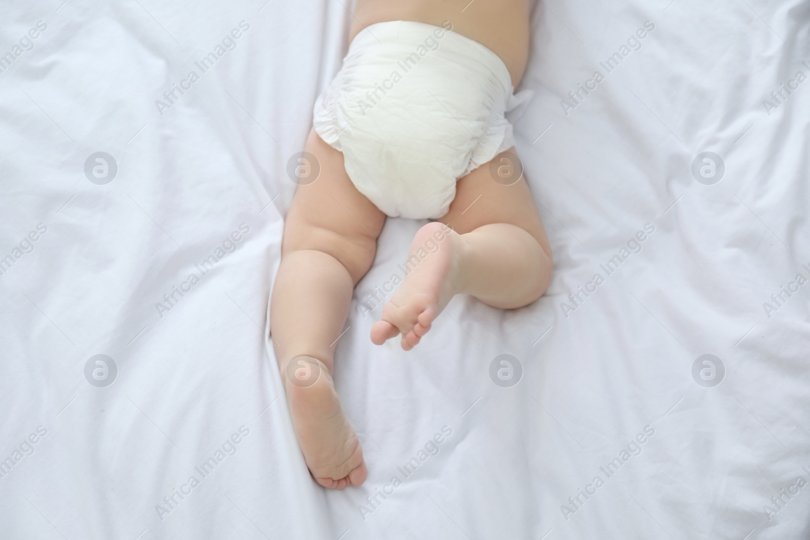 Photo of Cute little baby in diaper on bed, top view