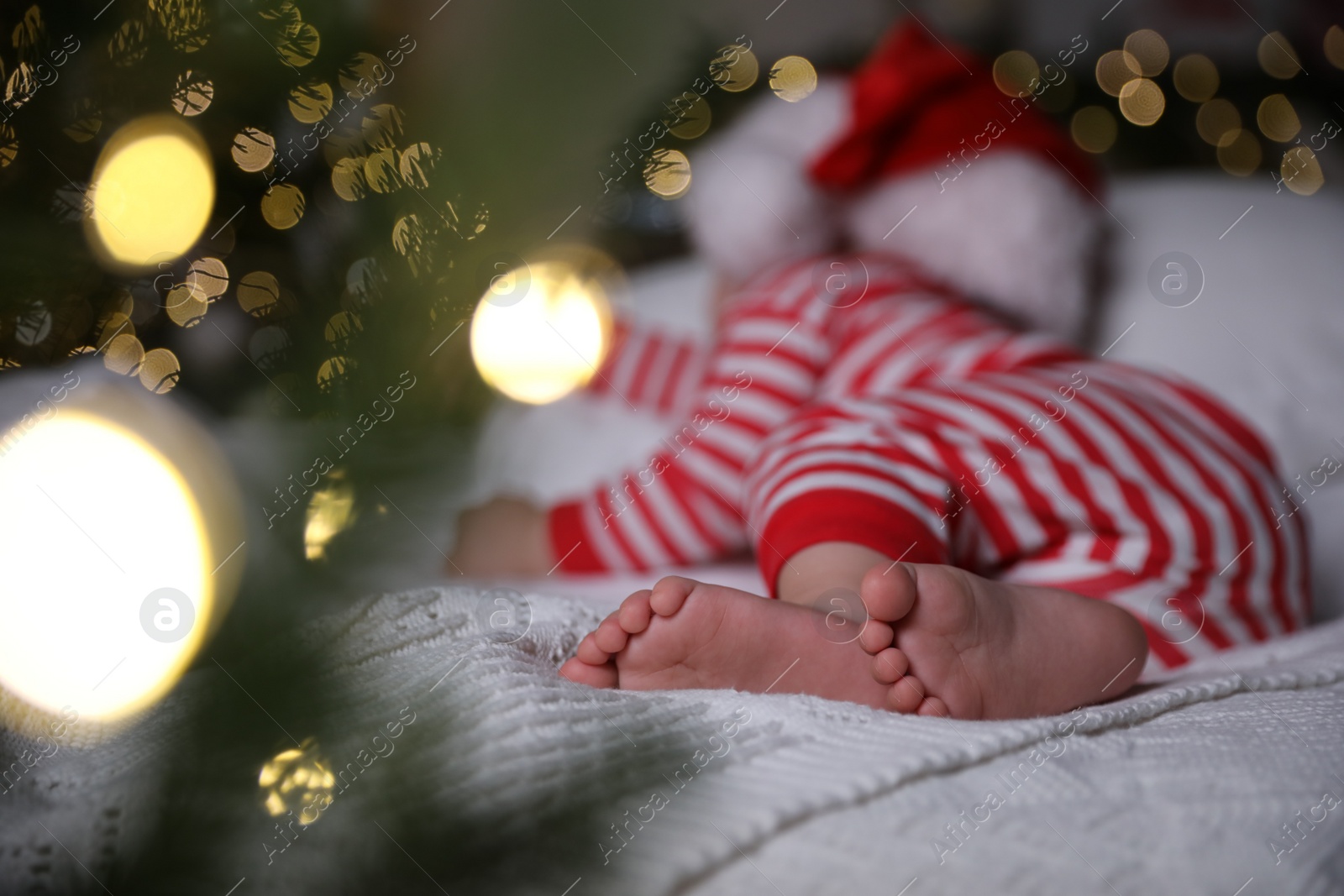 Photo of Baby in Christmas pajamas and Santa hat sleeping on bed indoors, focus on feet