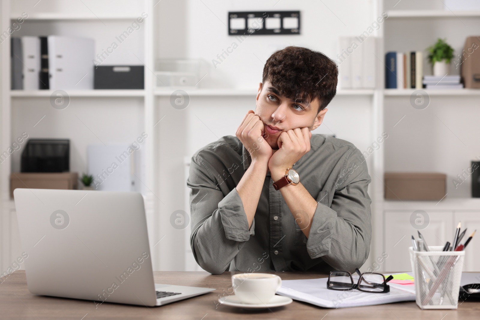 Photo of Tired young man working at table in office. Deadline concept