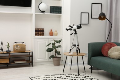 Photo of Tripod with modern telescope on table in living room