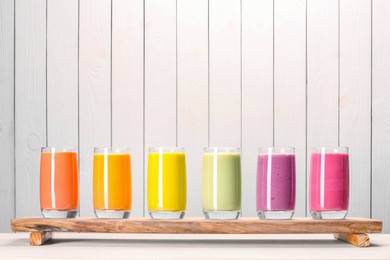 Photo of Board with many different tasty smoothies against white wooden background, space for text