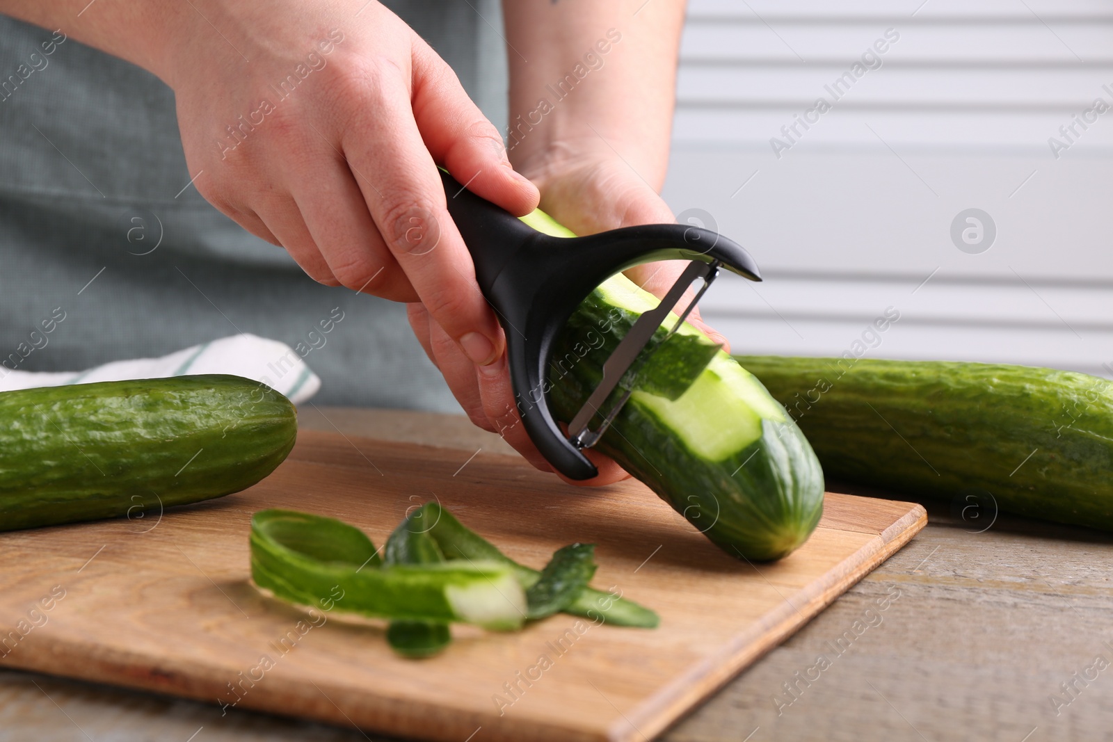 Photo of Woman peeling cucumber at wooden table indoors, closeup