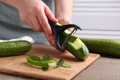 Photo of Woman peeling cucumber at wooden table indoors, closeup