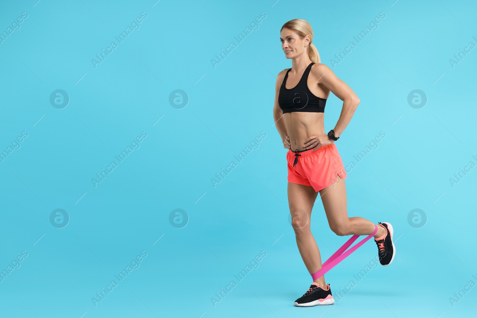 Photo of Woman exercising with elastic resistance band on light blue background. Space for text