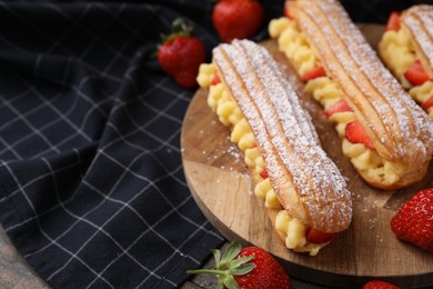 Photo of Delicious eclairs filled with cream and strawberries on table, closeup. Space for text