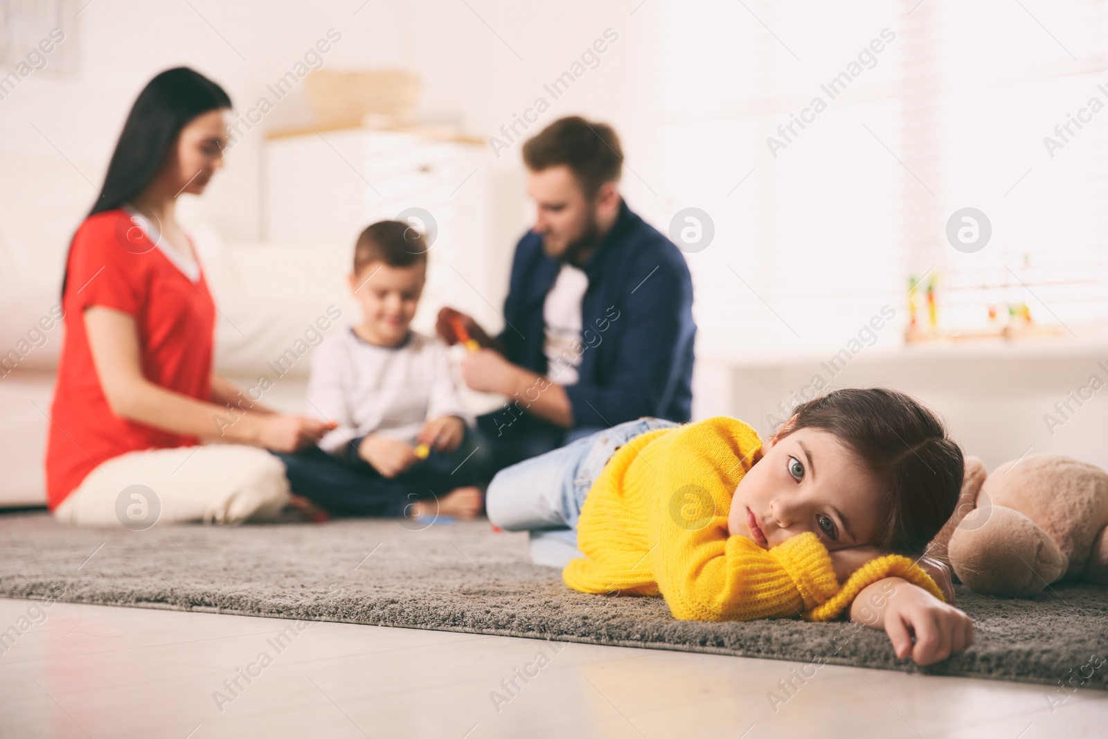 Photo of Unhappy little girl feeling jealous while parents spending time with her brother at home