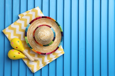Mexican sombrero hat, towel and maracas on blue wooden surface, top view. Space for text