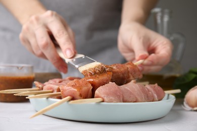 Photo of Woman spreading marinade onto raw meat with basting brush at table, closeup