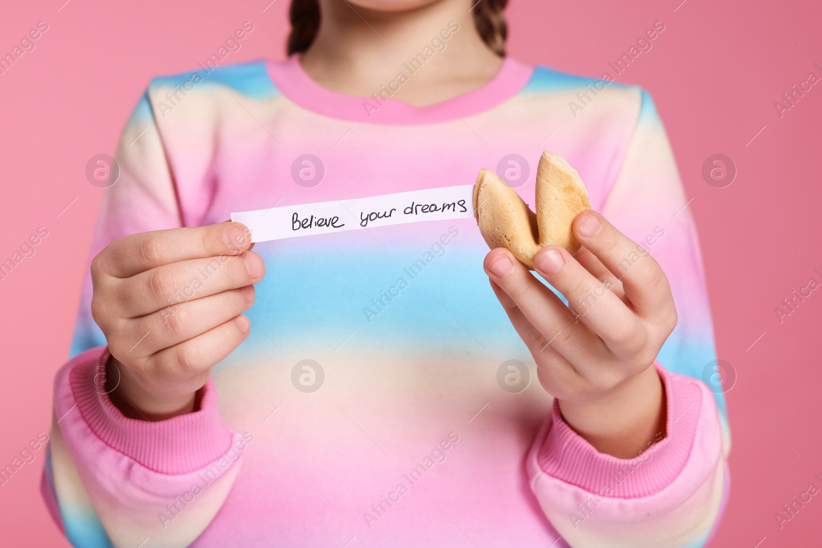 Photo of Girl holding tasty fortune cookie and prediction on pink background, closeup