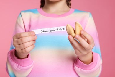 Girl holding tasty fortune cookie and prediction on pink background, closeup