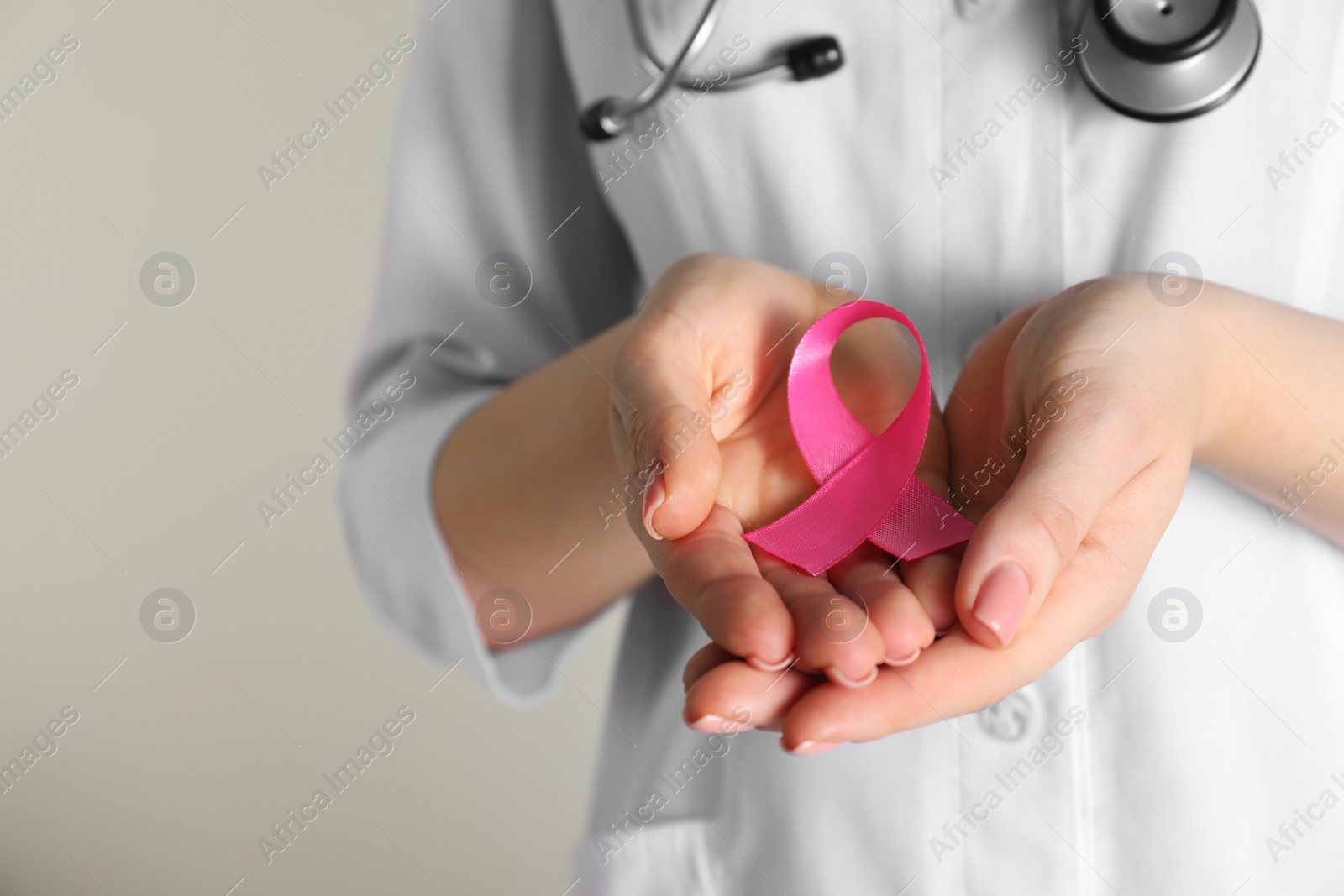 Photo of Mammologist with pink ribbon on light background, closeup. Breast cancer awareness