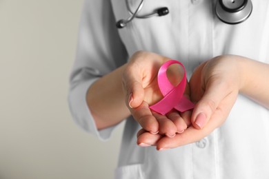 Photo of Mammologist with pink ribbon on light background, closeup. Breast cancer awareness