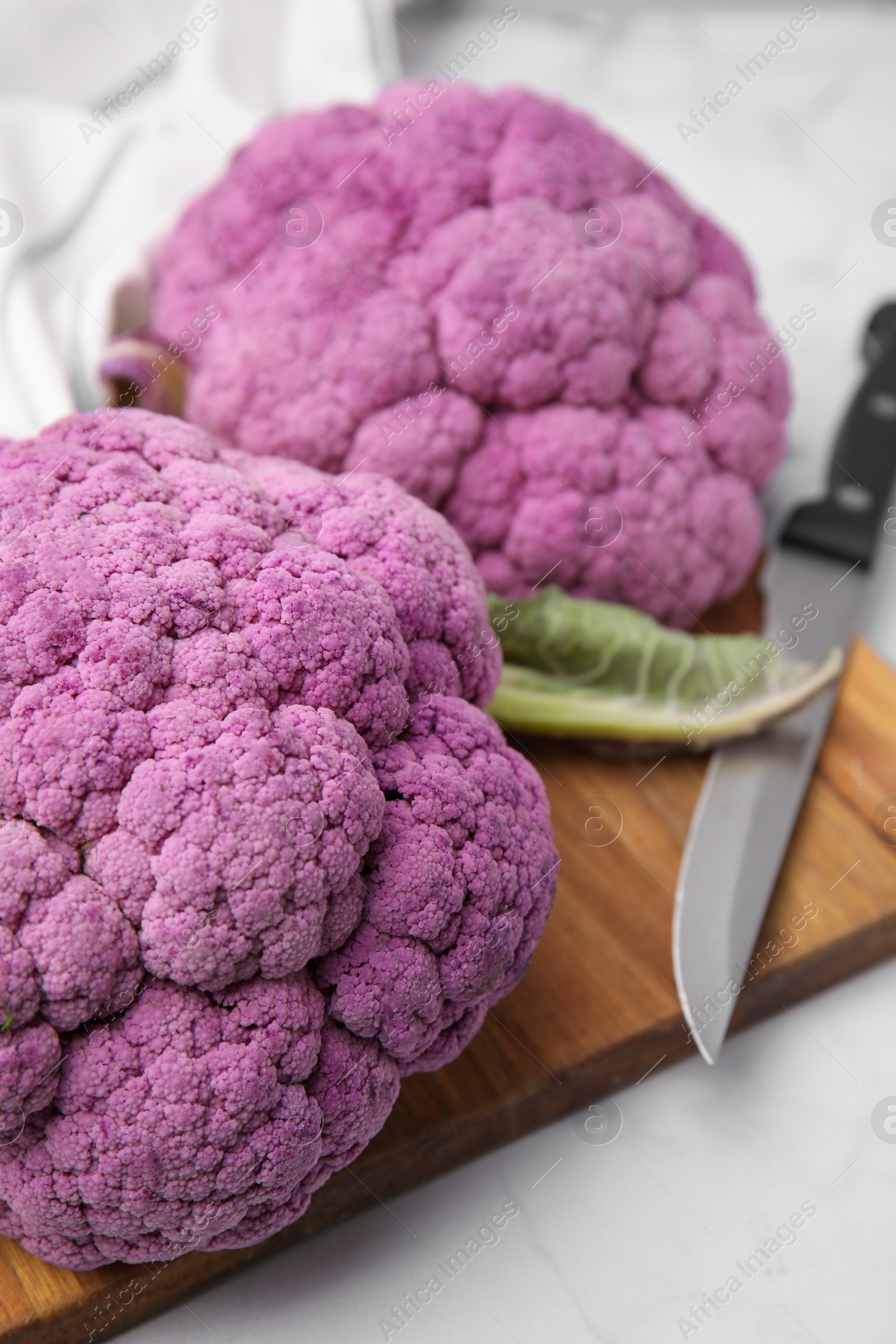 Photo of Fresh cauliflowers, cutting board and knife on white table, closeup