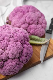 Photo of Fresh cauliflowers, cutting board and knife on white table, closeup