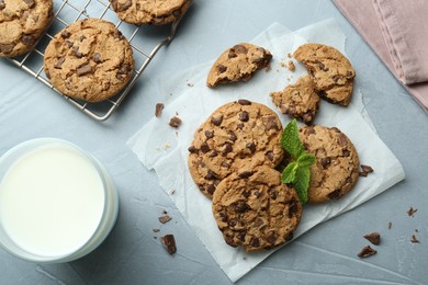 Photo of Tasty chocolate chip cookies, glass of milk and mint leaves on light grey table, flat lay