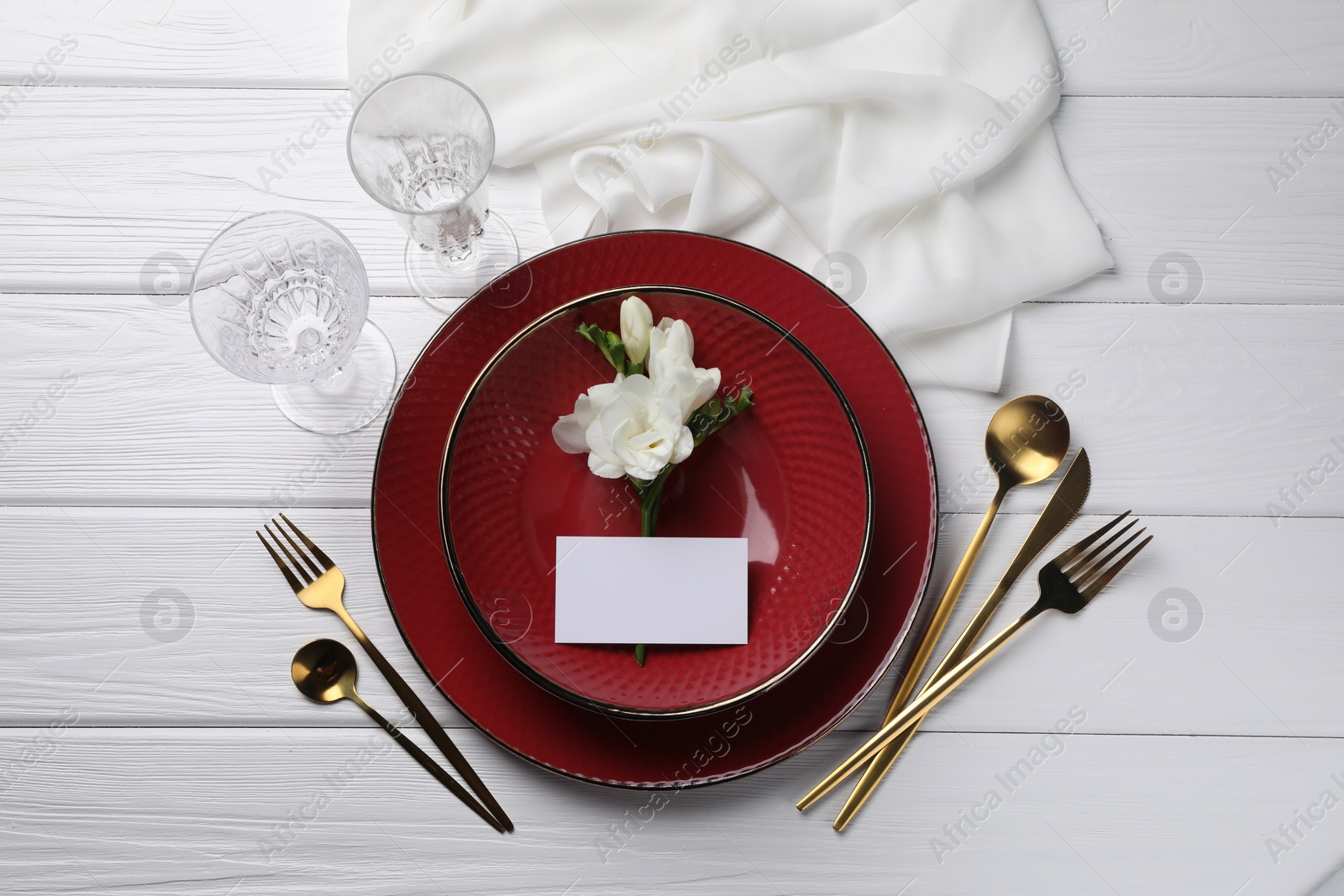 Photo of Stylish table setting. Dishes, cutlery, blank card and floral decor on white wooden background, flat lay