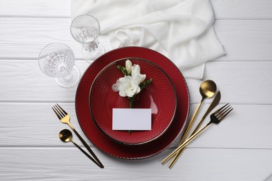 Photo of Stylish table setting. Dishes, cutlery, blank card and floral decor on white wooden background, flat lay