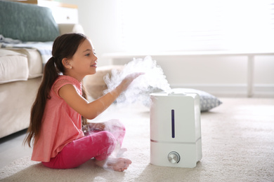 Photo of Little girl near modern air humidifier at home