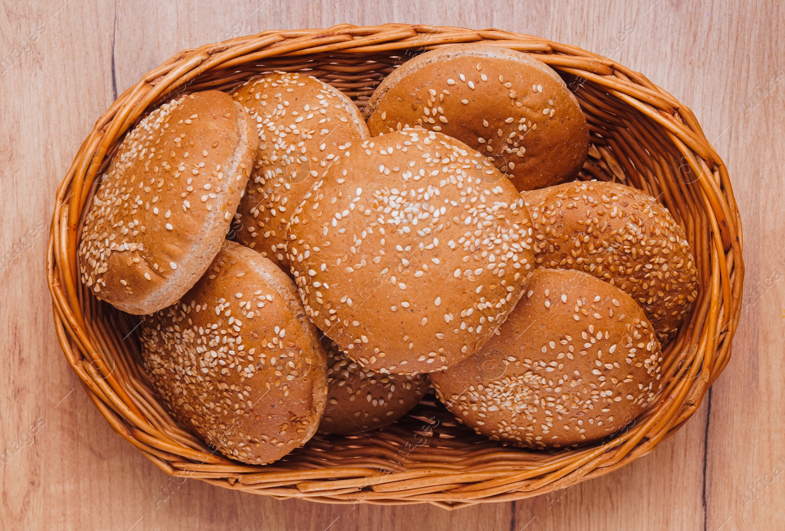 Photo of Wicker basket of fresh buns with sesame seeds on wooden table, top view