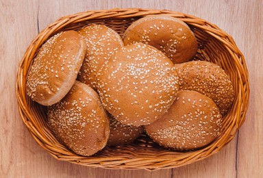 Photo of Wicker basket of fresh buns with sesame seeds on wooden table, top view