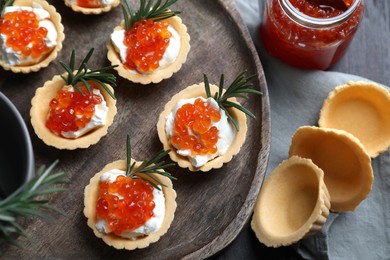 Photo of Delicious tartlets with red caviar and cream cheese served on wooden table, flat lay
