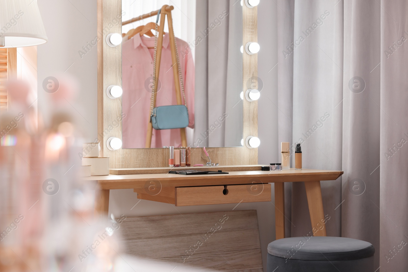 Photo of Stylish mirror with light bulbs and beauty products on wooden dressing table in makeup room