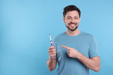 Photo of Happy man holding electric toothbrush on light blue background. Space for text