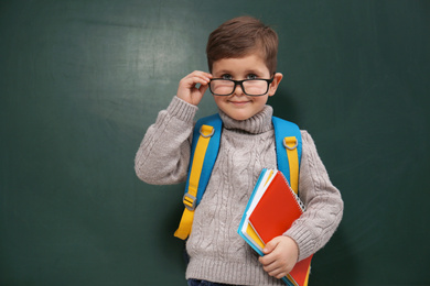 Photo of Cute little child wearing glasses near chalkboard. First time at school