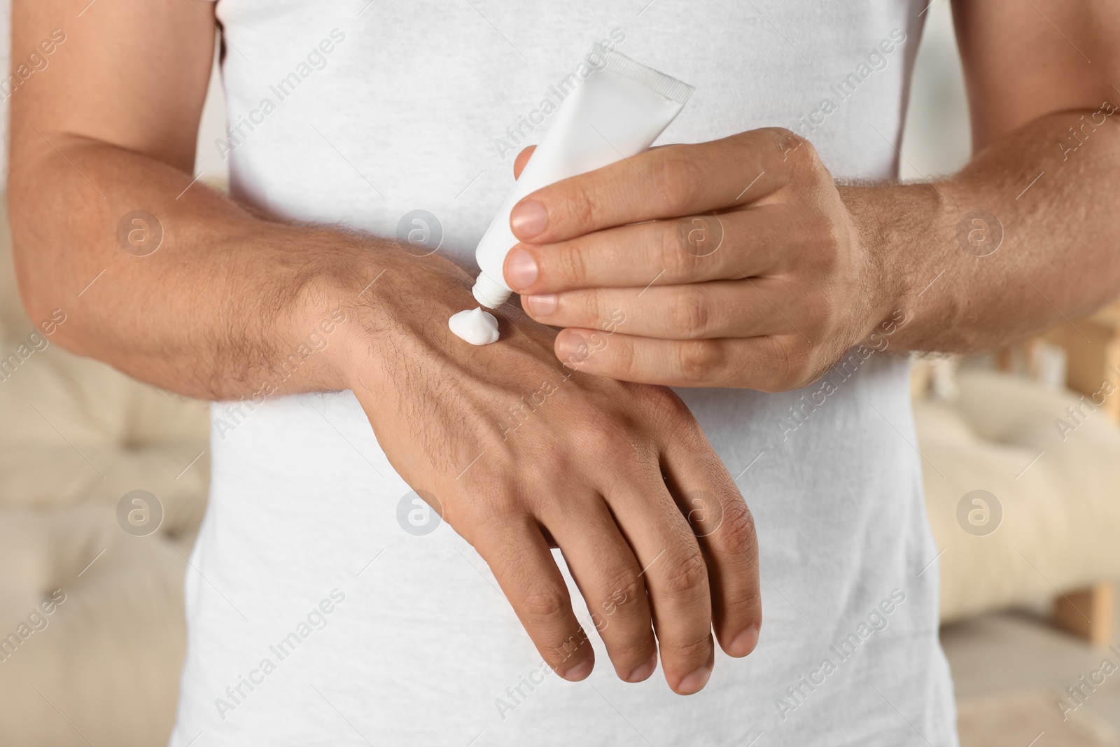 Photo of Man applying cream from tube onto hand indoors, closeup