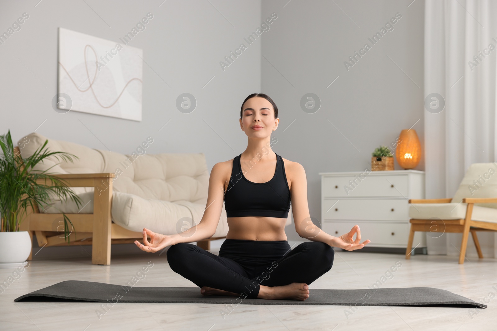 Photo of Beautiful young woman practicing Padmasana on yoga mat at home. Lotus pose