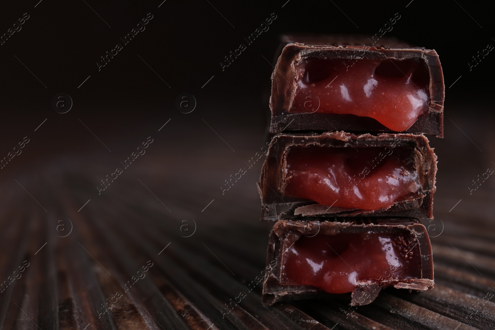 Photo of Tasty dark chocolate candies with liquid filling on wooden board, closeup. Space for text