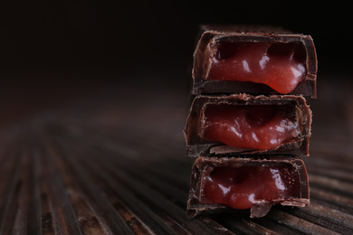 Photo of Tasty dark chocolate candies with liquid filling on wooden board, closeup. Space for text