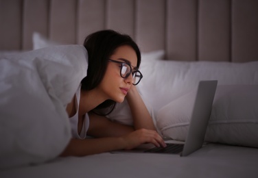 Photo of Young woman with nomophobia using laptop in bed at night. Insomnia concept
