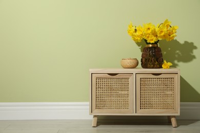 Beautiful daffodils in vase on table near light green wall indoors, space for text