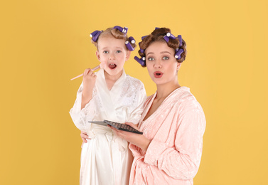 Photo of Emotional daughter and mother with cosmetic on yellow background