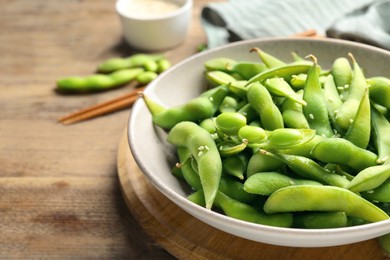 Photo of Green edamame beans in pods served on wooden table, closeup. Space for text